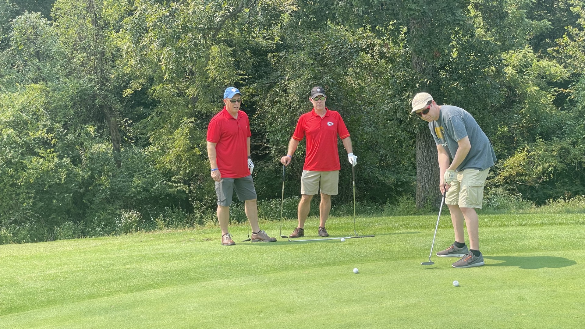 A golfer lines up a putt while two playing partners watch from the edge of the green